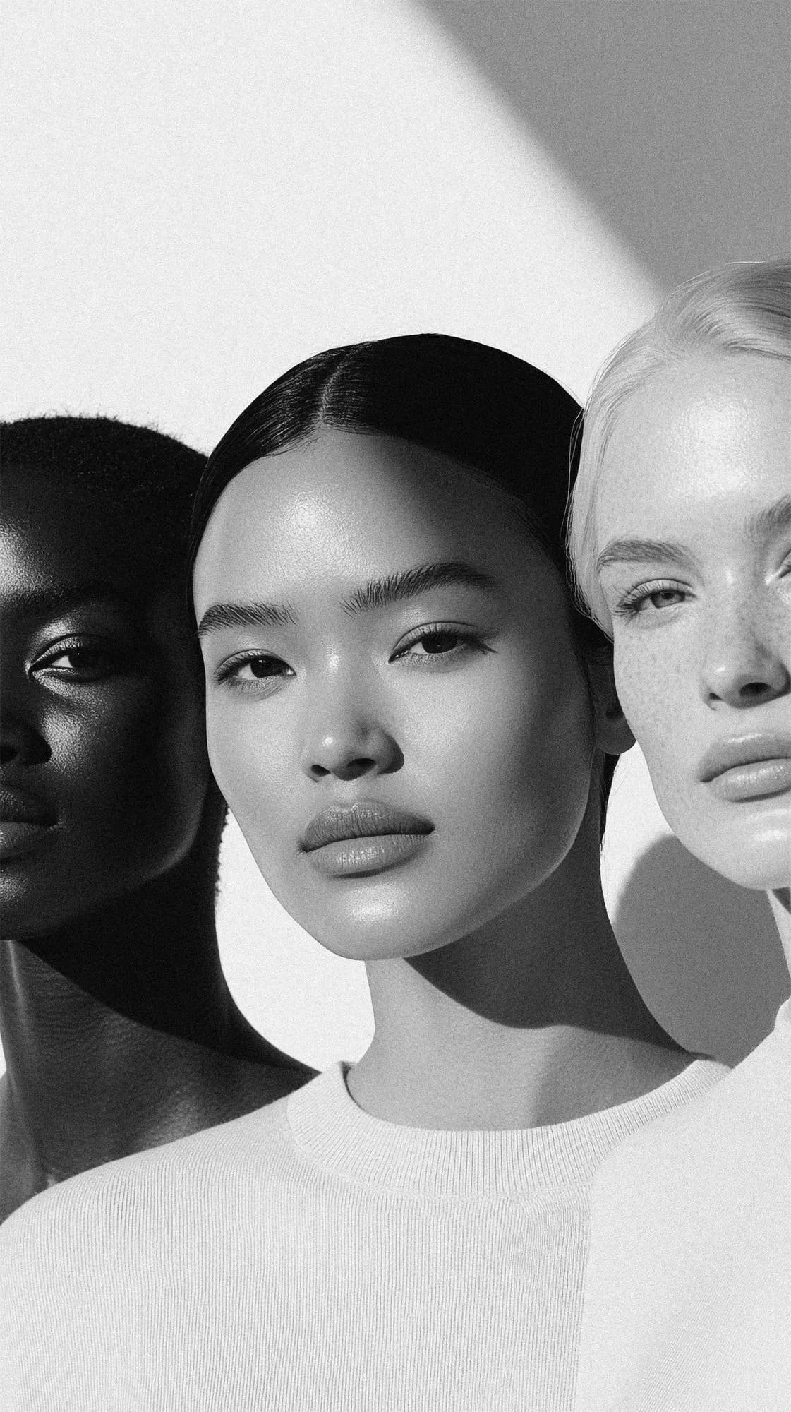 Three faces side by side in black and white, skin lit softly from above
