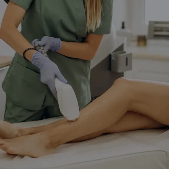 A practitioner in green scrubs passing a laser handpiece over a lower leg
