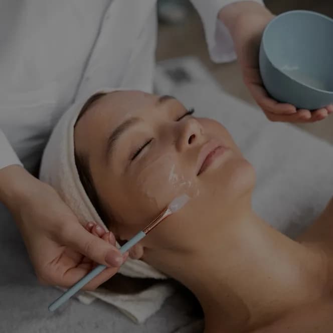 A peel being brushed onto a client’s cheek from a small bowl